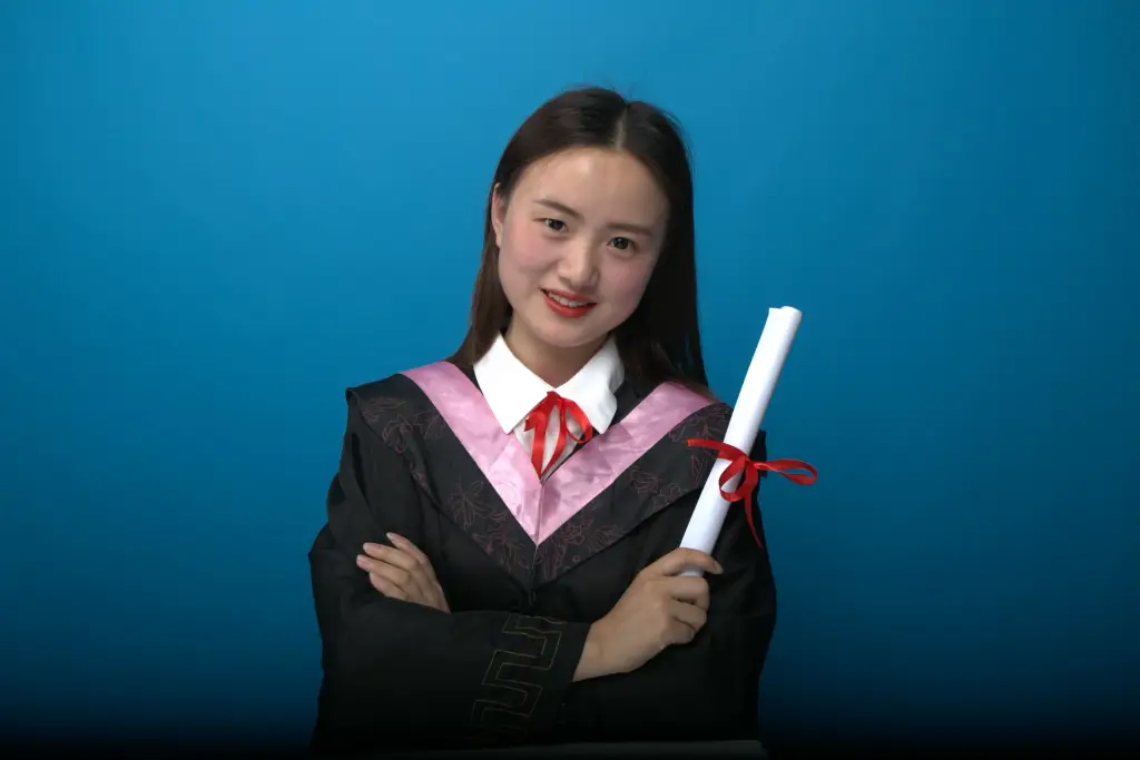 Confident graduate in cap and gown with diploma, blue backdrop.