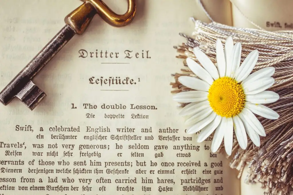 A vintage key and daisy rest on an antique book page, evoking nostalgia and elegance.