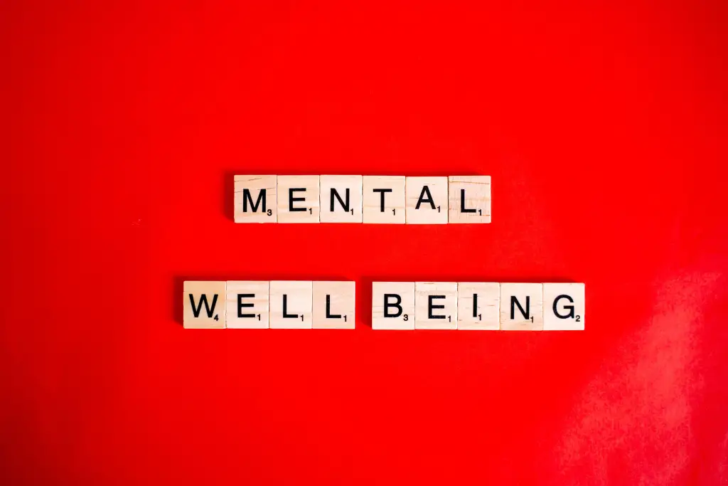 Wooden Scrabble tiles spelling 'mental wellbeing' on a vibrant red background.