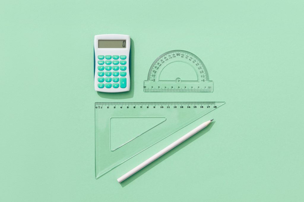 A minimalist flat lay of school supplies on a green background including a calculator, rulers, and pencil.