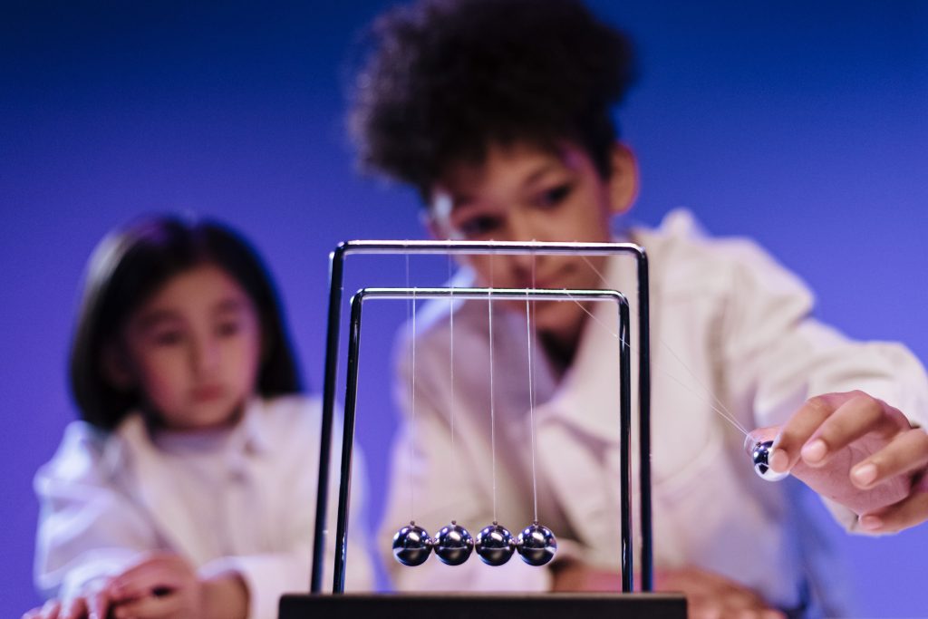 A boy and a girl engaged with a Newton's Cradle in a science setting, showcasing curiosity and learning.