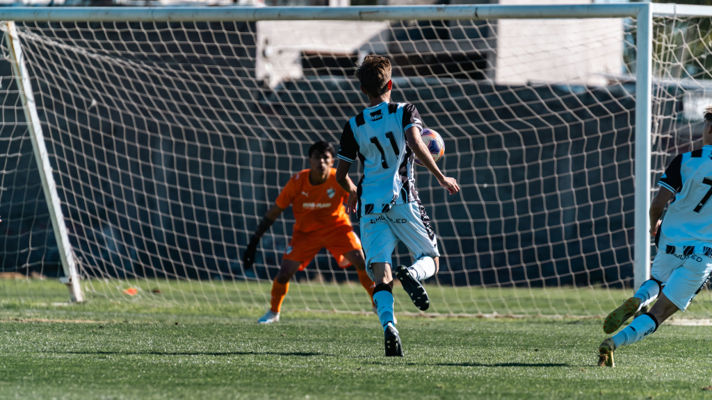 A soccer player attempts to score a goal while the goalie prepares to block the shot.